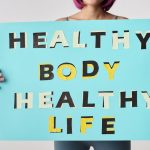 A woman holds a motivational poster advocating a healthy body and life for wellness.