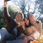 Happy family taking a selfie during a sunny picnic in a park.